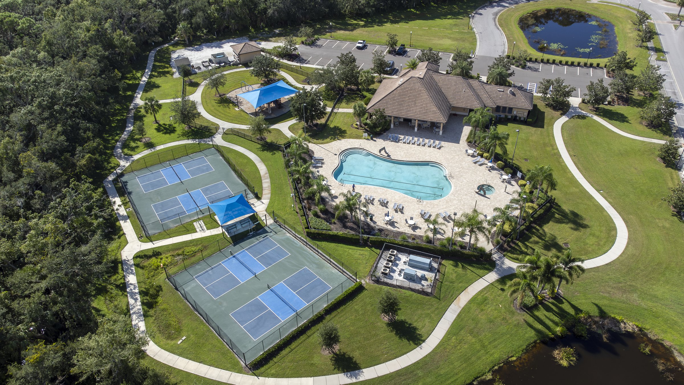Aerial of community clubhouse, pool, and tennis courts with pond — Sarasota Florida drone photography